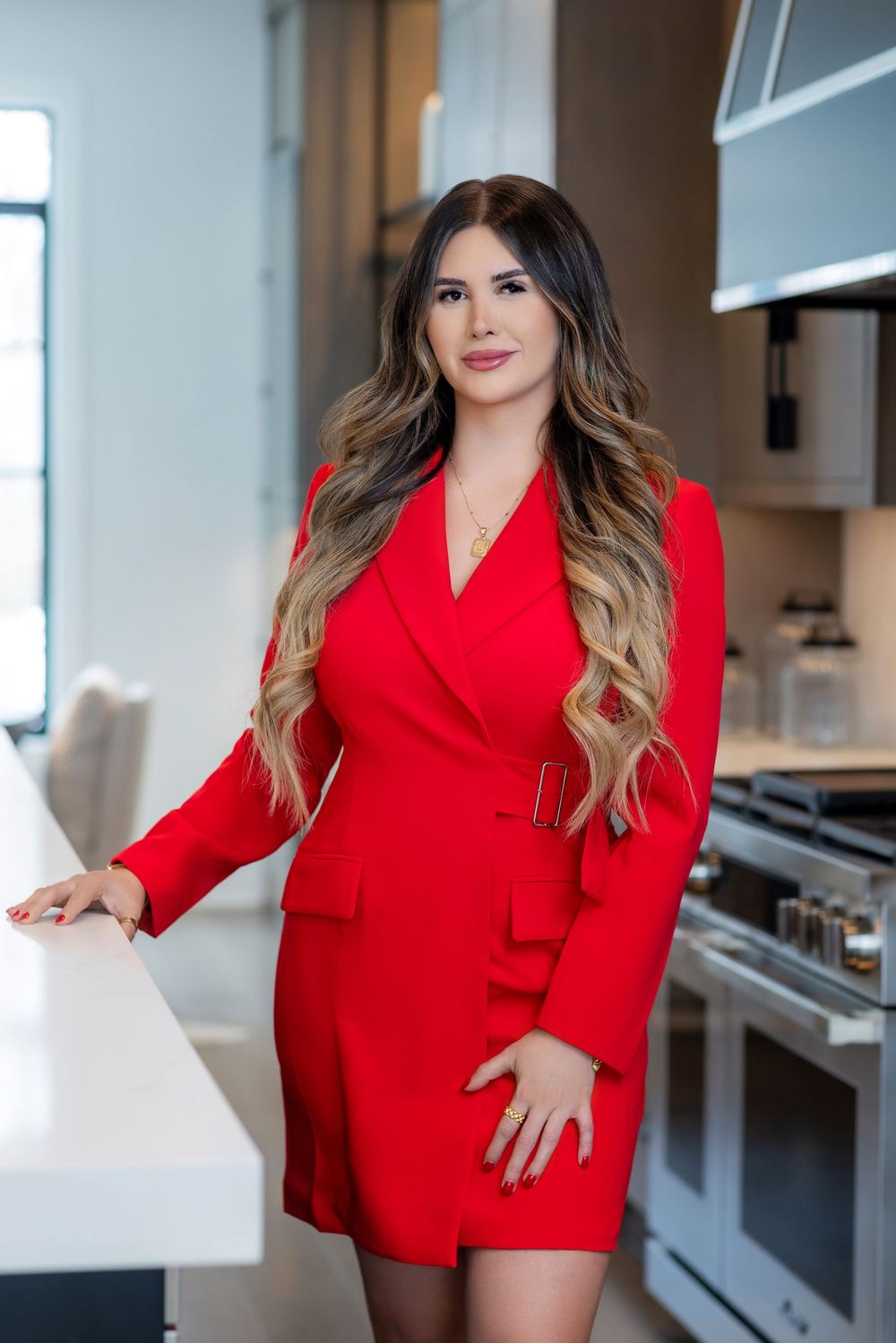 A person in a stylish red blazer dress poses confidently in a modern kitchen setting.