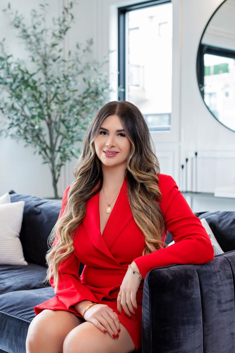 Lifestyle photoshoot featuring a red blazer dress on a dark couch with decorative plants in the background.