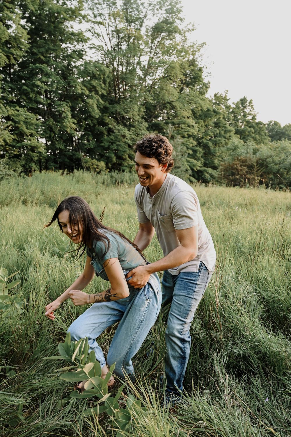 A playful moment between two people enjoying time together in a lush green field on a sunny day.