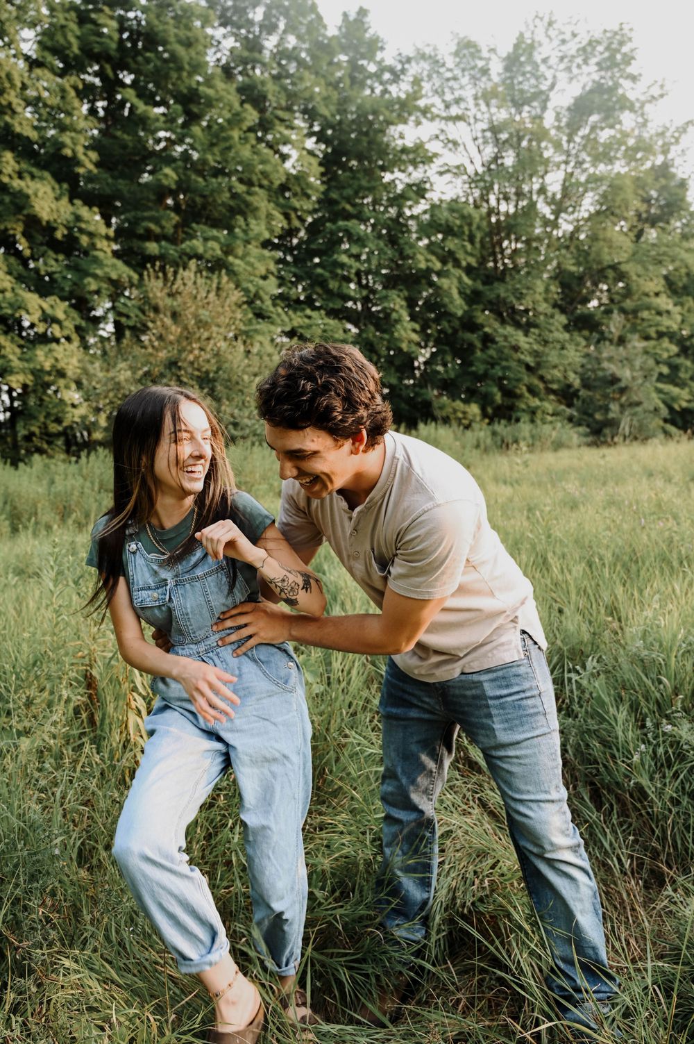 A playful candid moment shared between two people laughing together in a grassy field during golden hour.