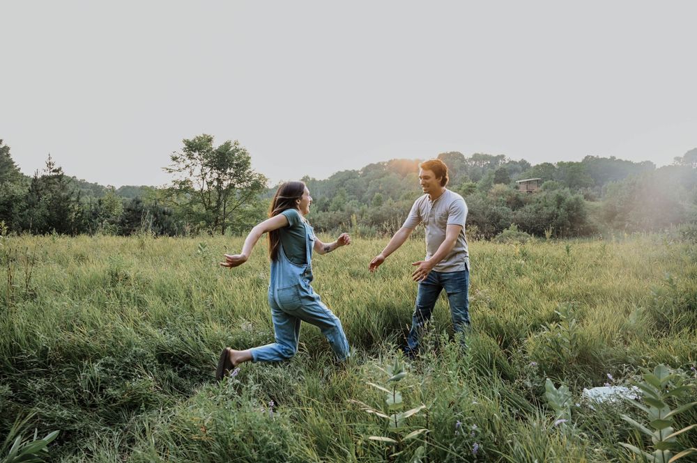 People playfully run together through a sunny meadow with tall grass during golden hour.