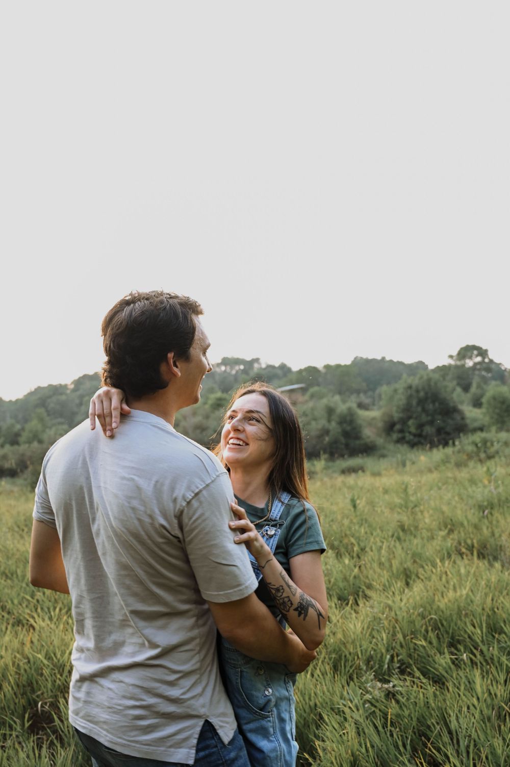 A romantic scene of a couple embracing in a sunlit meadow with green trees in the background.