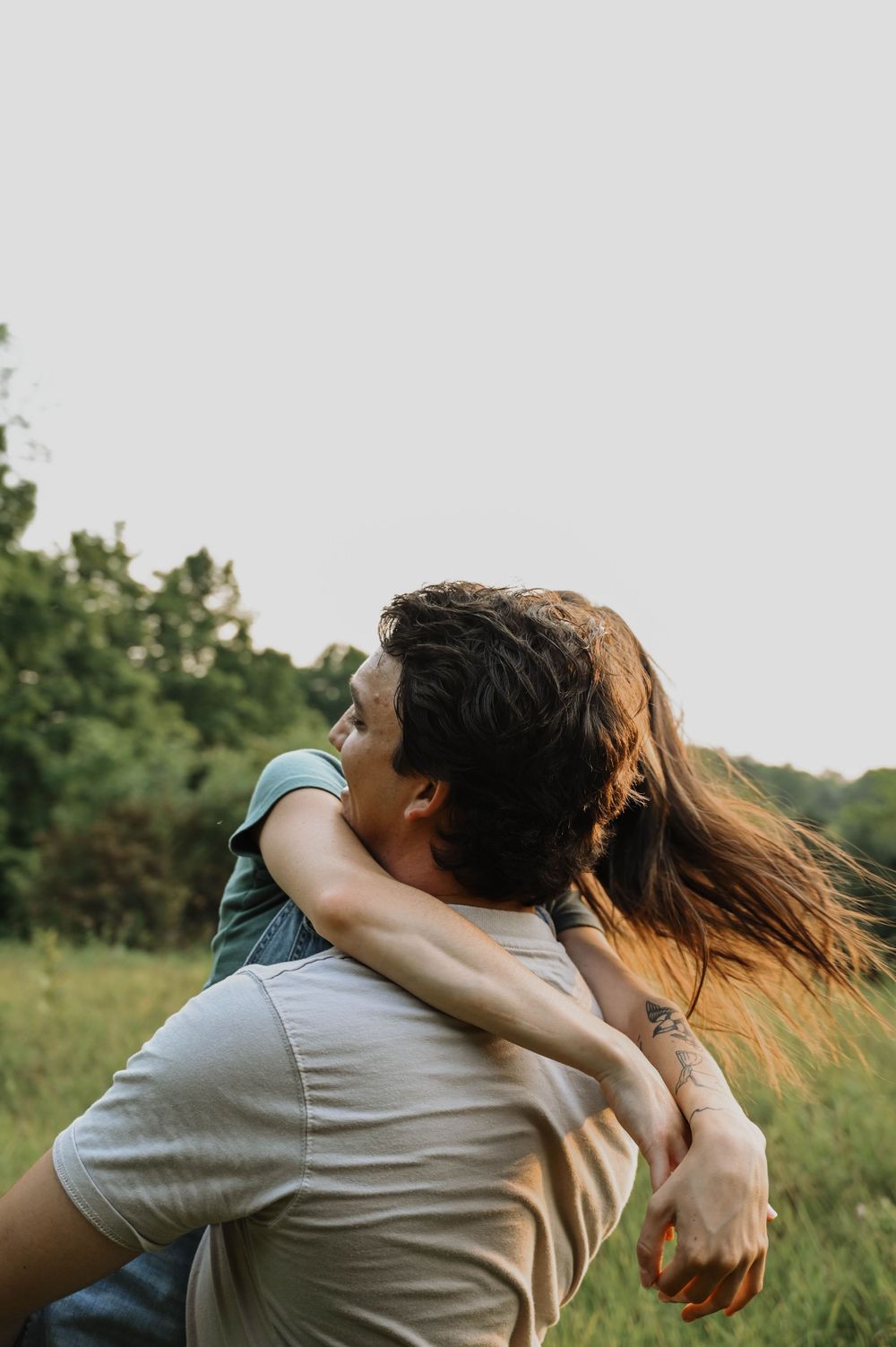 A romantic embrace in a grassy field at golden hour with sunlight illuminating flowing hair and natural scenery.