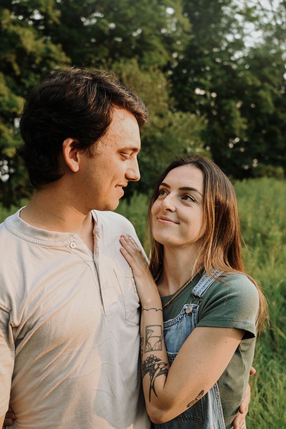 A young couple embraces outdoors in a natural setting with green foliage in the background.