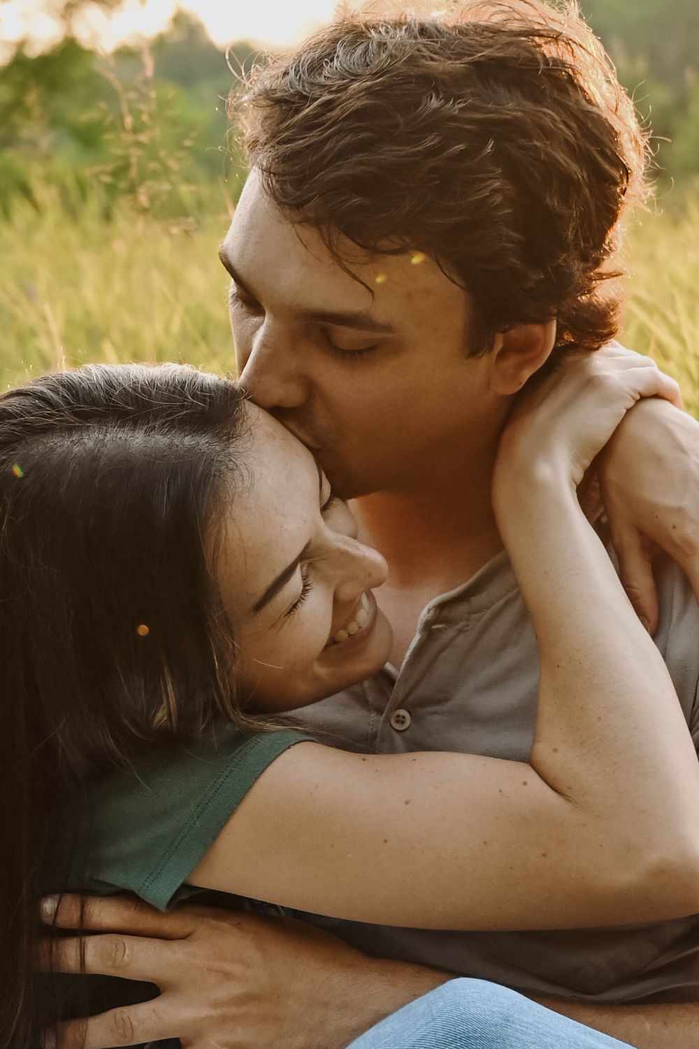 A tender moment between two people embracing in a sunlit meadow with a warm golden glow during sunset.