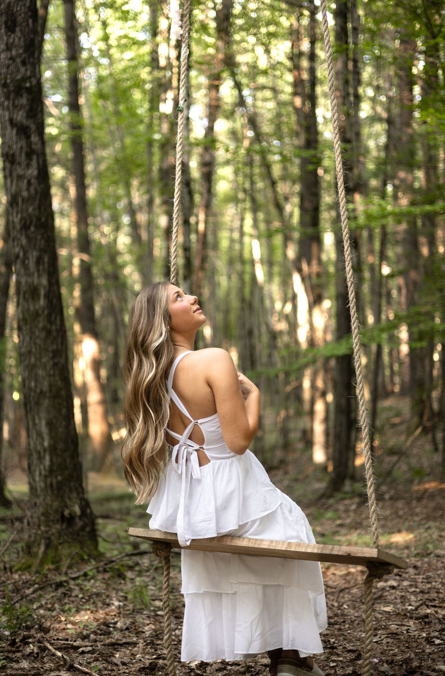 A dreamy woodland scene with a wooden swing and flowing white dress against a backdrop of sunlit forest trees.