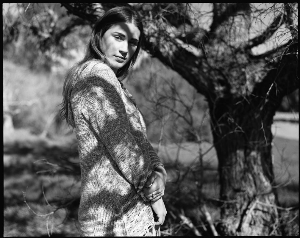 Moody black and white portrait amidst trees with dramatic natural lighting effects.