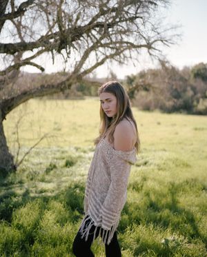 Artistic portrait in a grassy field under a gnarled tree branch wearing a knit sweater.