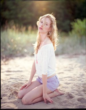 Dreamy beach portrait in white top and shorts with golden sunset lighting.