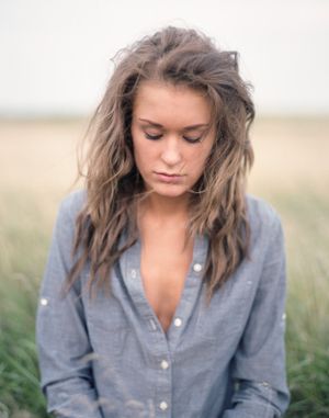 Moody portrait in chambray shirt against rustic field backdrop.