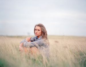 Serene portrait in tall grass field wearing casual denim outfit.