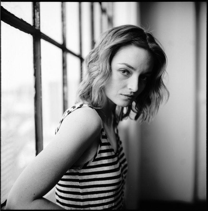 Black and white portrait in striped top near window with dramatic lighting.
