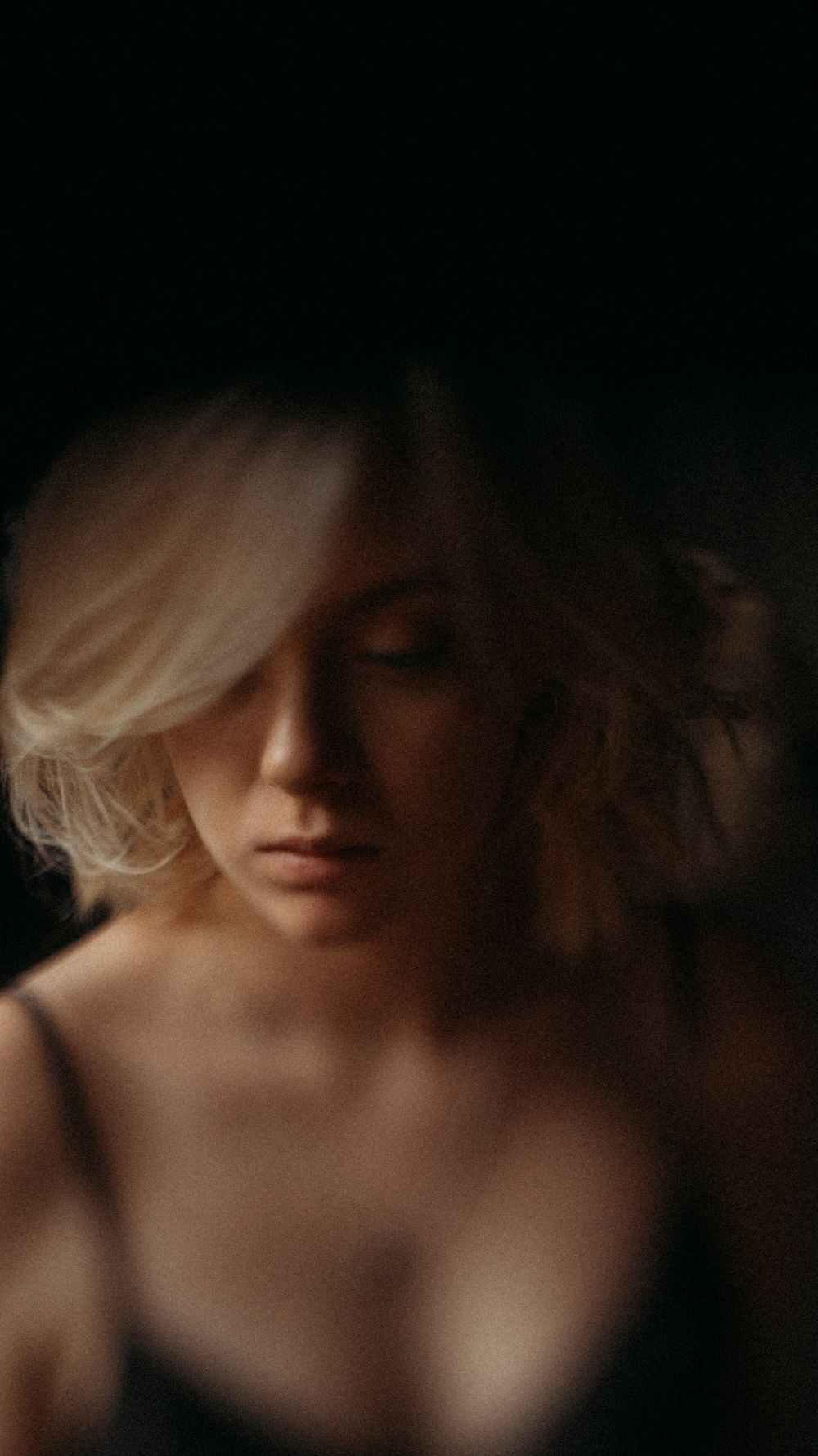 Soft focus portrait in dark tones with dramatic side lighting.