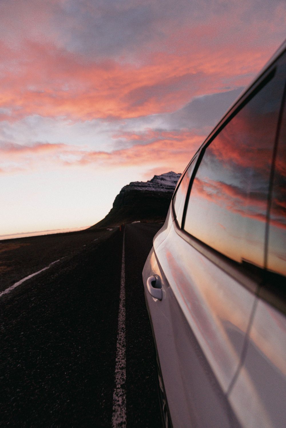 Vue latérale de la voiture conduisant sur une route de montagne pendant le coucher de soleil rose vibrant.