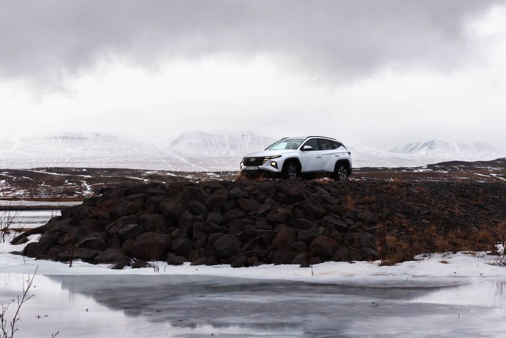 SUV blanc positionné sur un affleurement rocheux avec un paysage enneigé et un ciel nuageux en arrière-plan.
