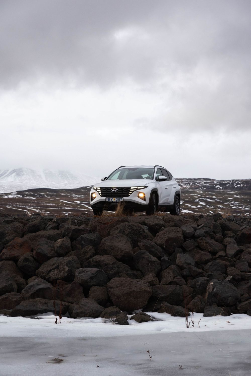 SUV Hyundai blanc perché sur un terrain rocheux avec de la neige et des montagnes au loin.