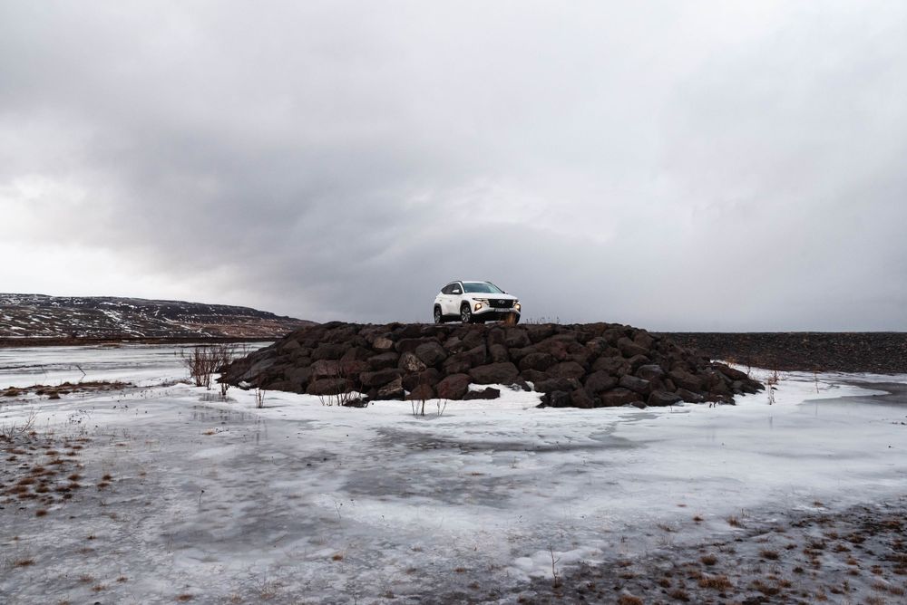 SUV garé au sommet d'une colline rocheuse entouré de neige et de glace sous un ciel gris de mauvaise humeur.
