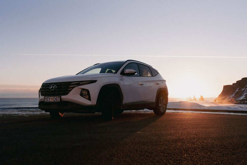 Silhouette de SUV Hyundai blanc contre un coucher de soleil spectaculaire sur la route côtière.