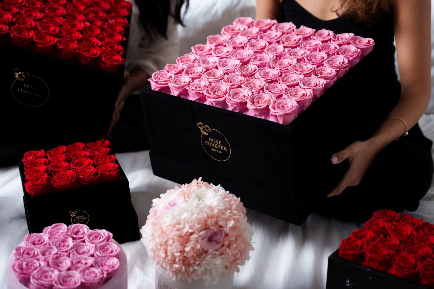 Luxury flower boxes filled with pink and red roses alongside a soft pink floral arrangement on white surface.