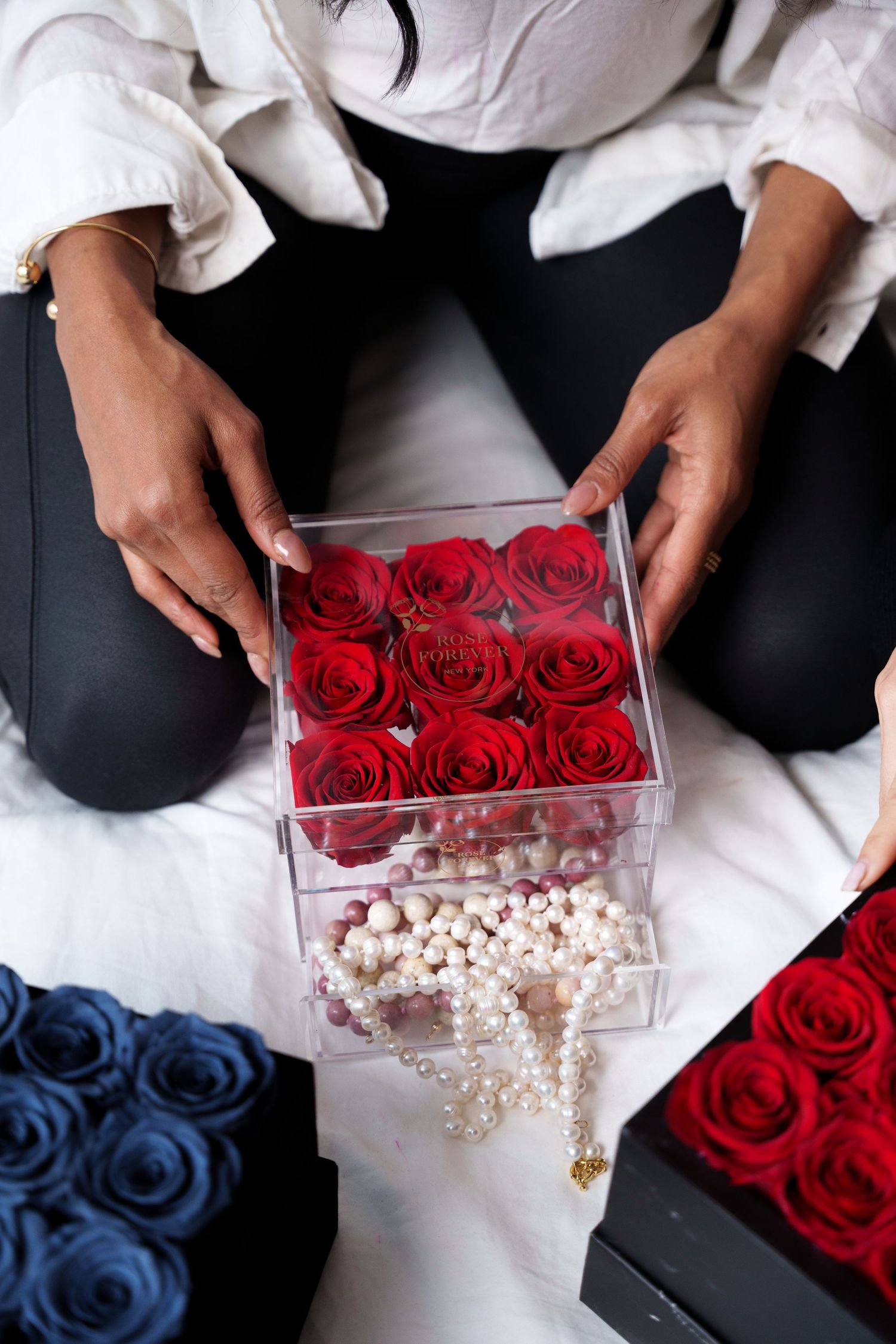 Hands arranging red roses in a clear acrylic box with white pearl decorations for elegant floral display.