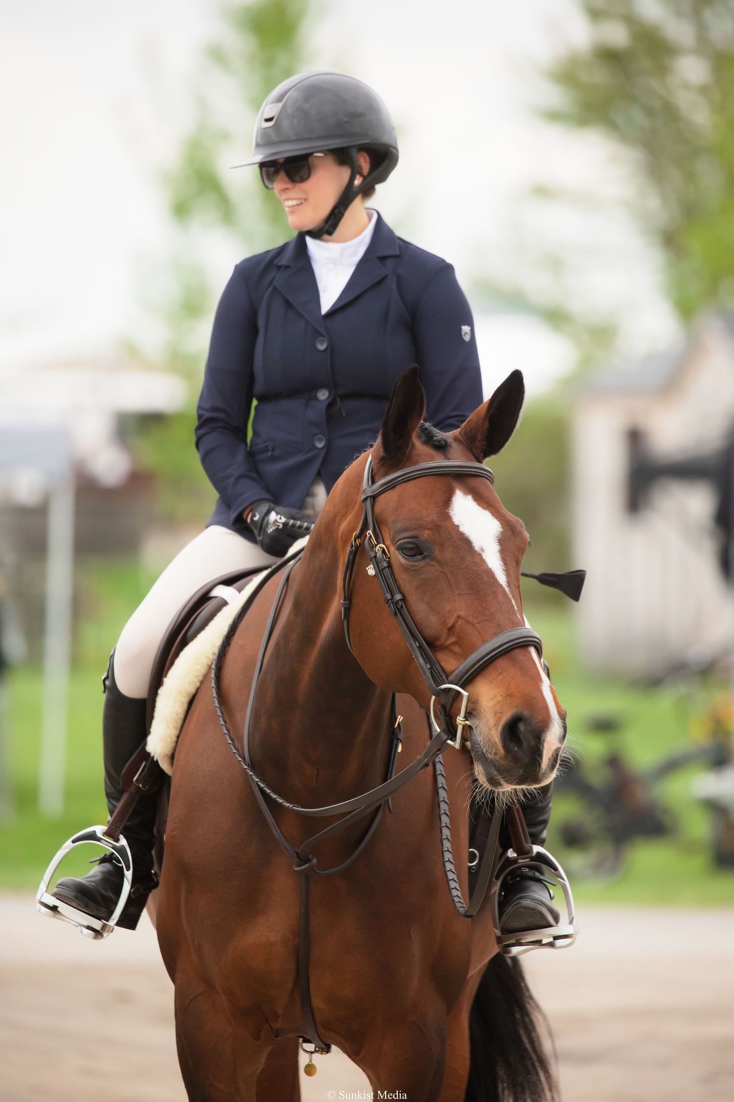 An equestrian rider in formal attire sits atop a brown horse with white markings during a competition.