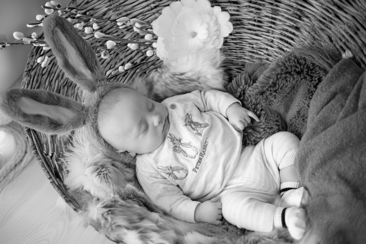 An infant sleeps peacefully in a white wicker bassinet surrounded by soft fabrics and blankets.