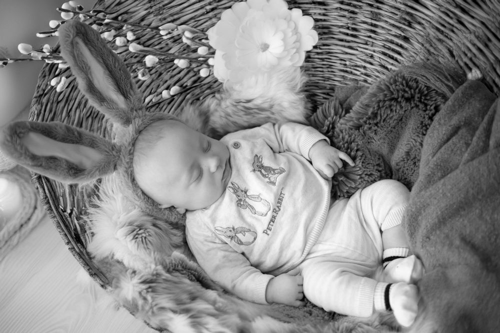 An infant sleeps peacefully in a white wicker bassinet surrounded by soft fabrics and blankets.