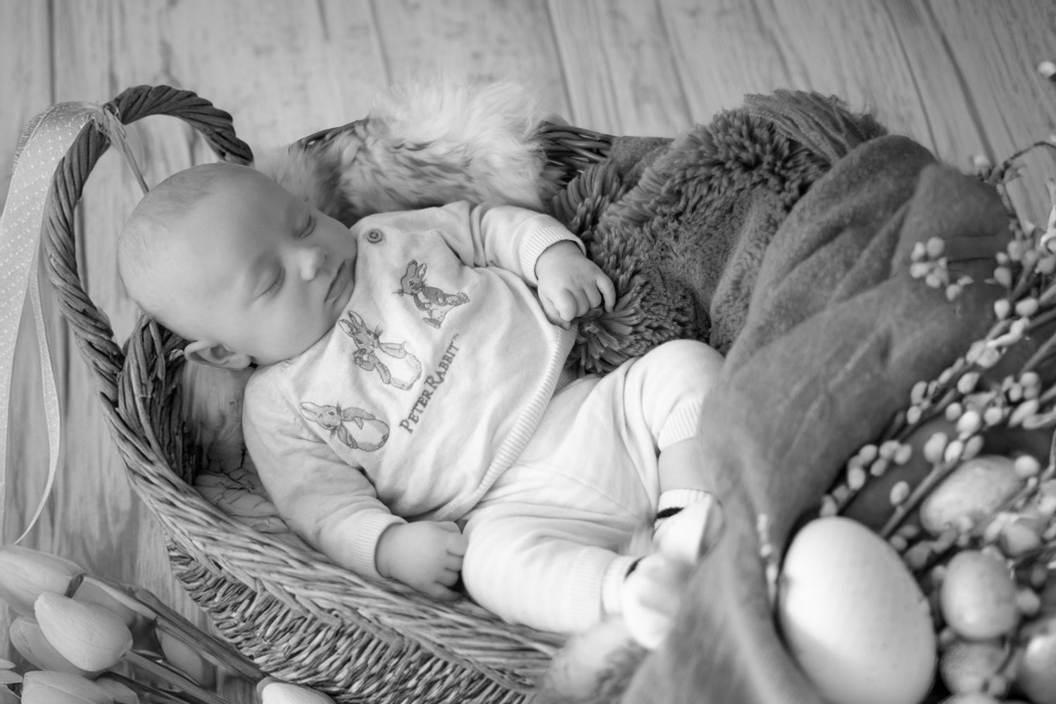 A sleeping baby lies in a wicker basket, surrounded by soft blankets and decorative springtime flowers.