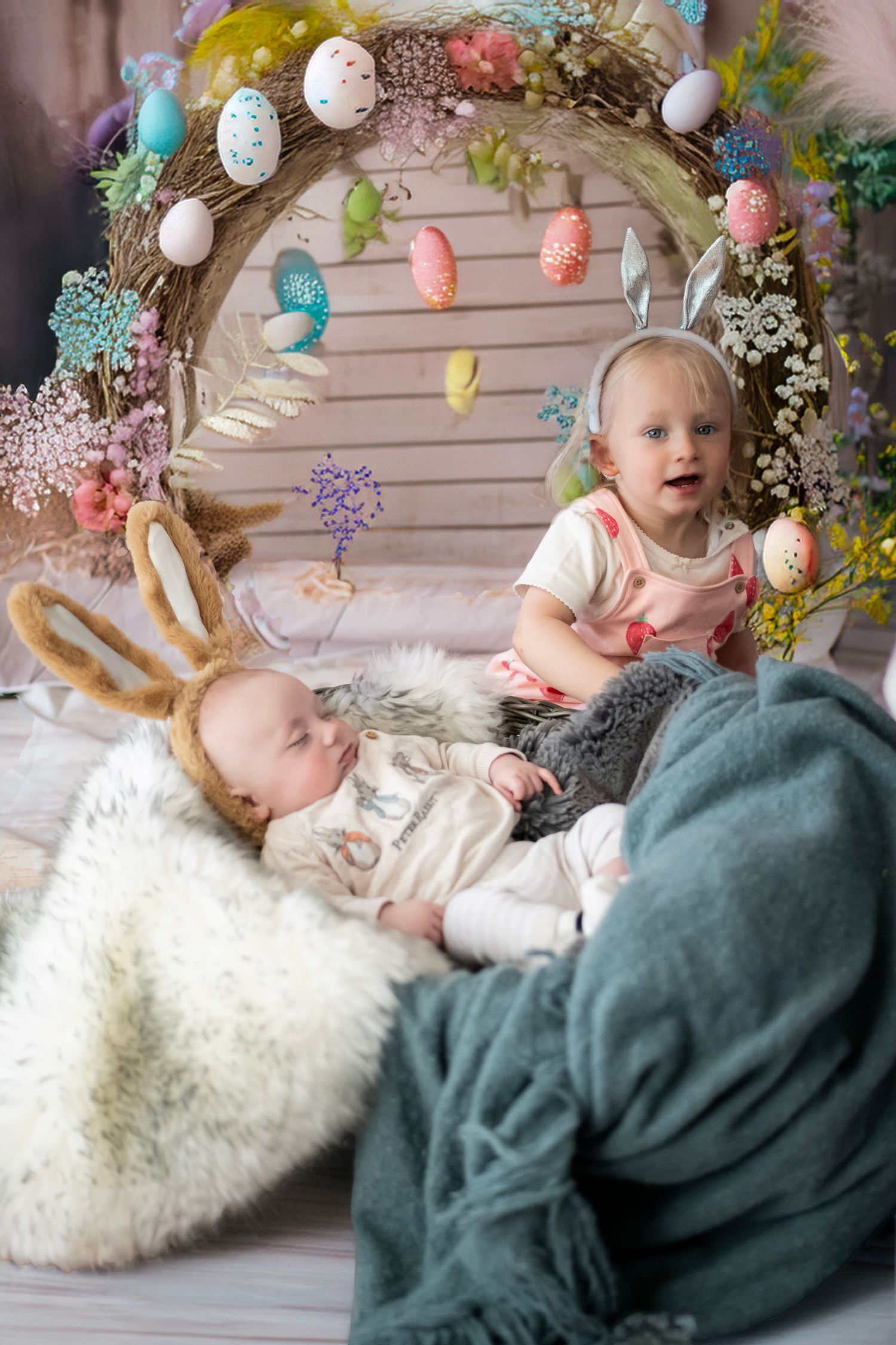 Easter themed photo setup with decorated arch, hanging eggs, and cozy blankets for spring portrait session.