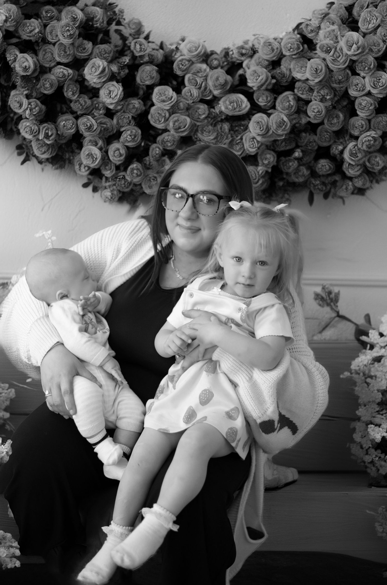 Black and white portrait with rose wall backdrop and comfortable seating arrangement.