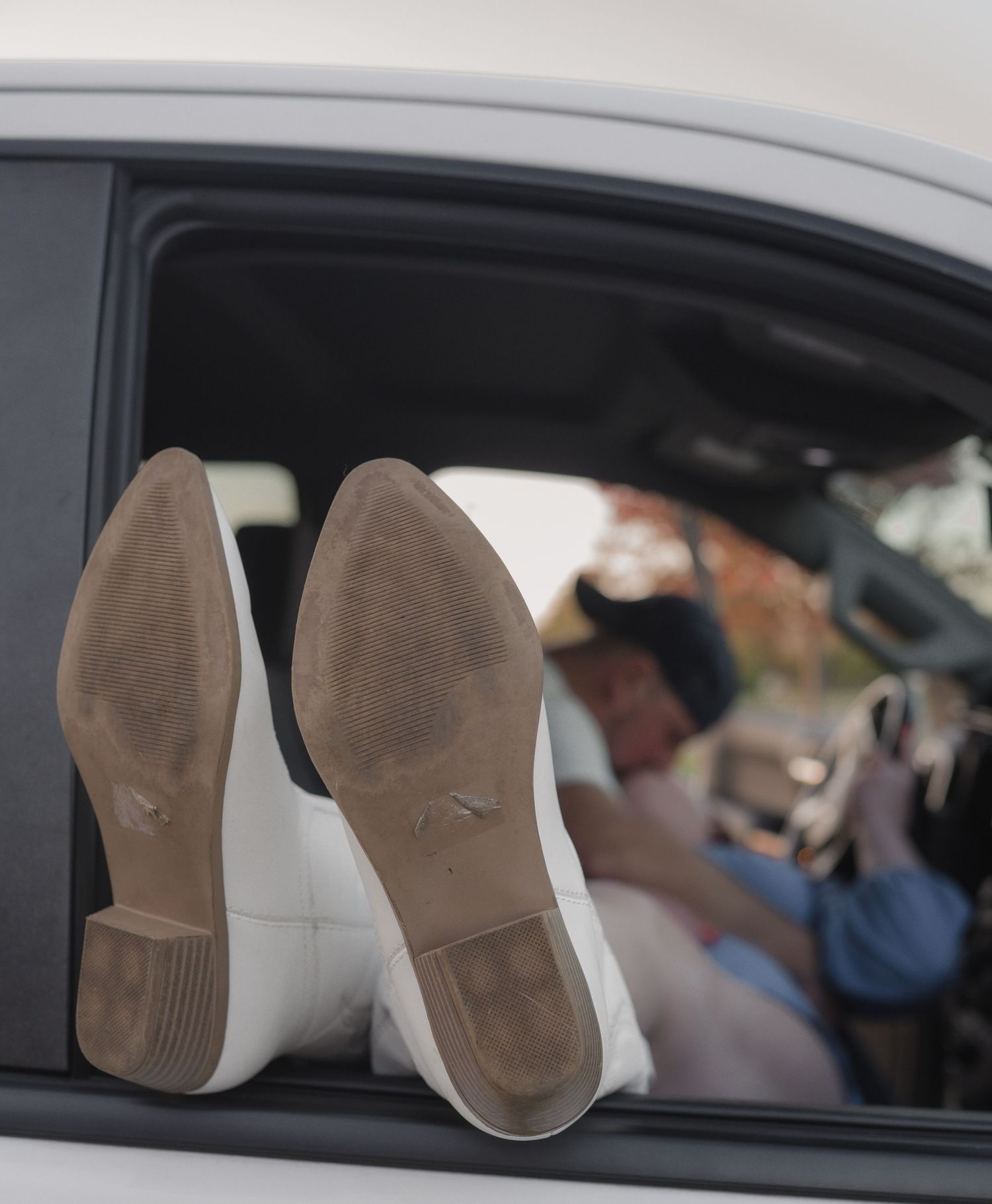 Two white sneakers resting on a car window with the soles facing outward in an artistic composition.