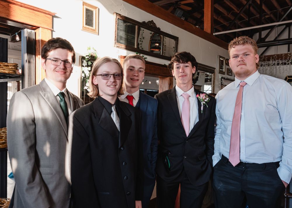 A group of formally dressed business professionals stand together in a restaurant interior with exposed beams.