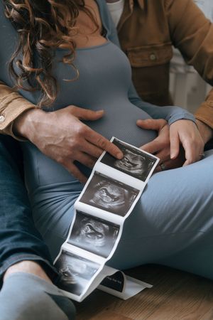 Expecting couple looking at ultrasound photos while sitting on wooden floor.