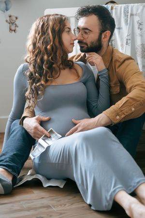 Couple in casual clothing sharing intimate moment while holding ultrasound images on floor.