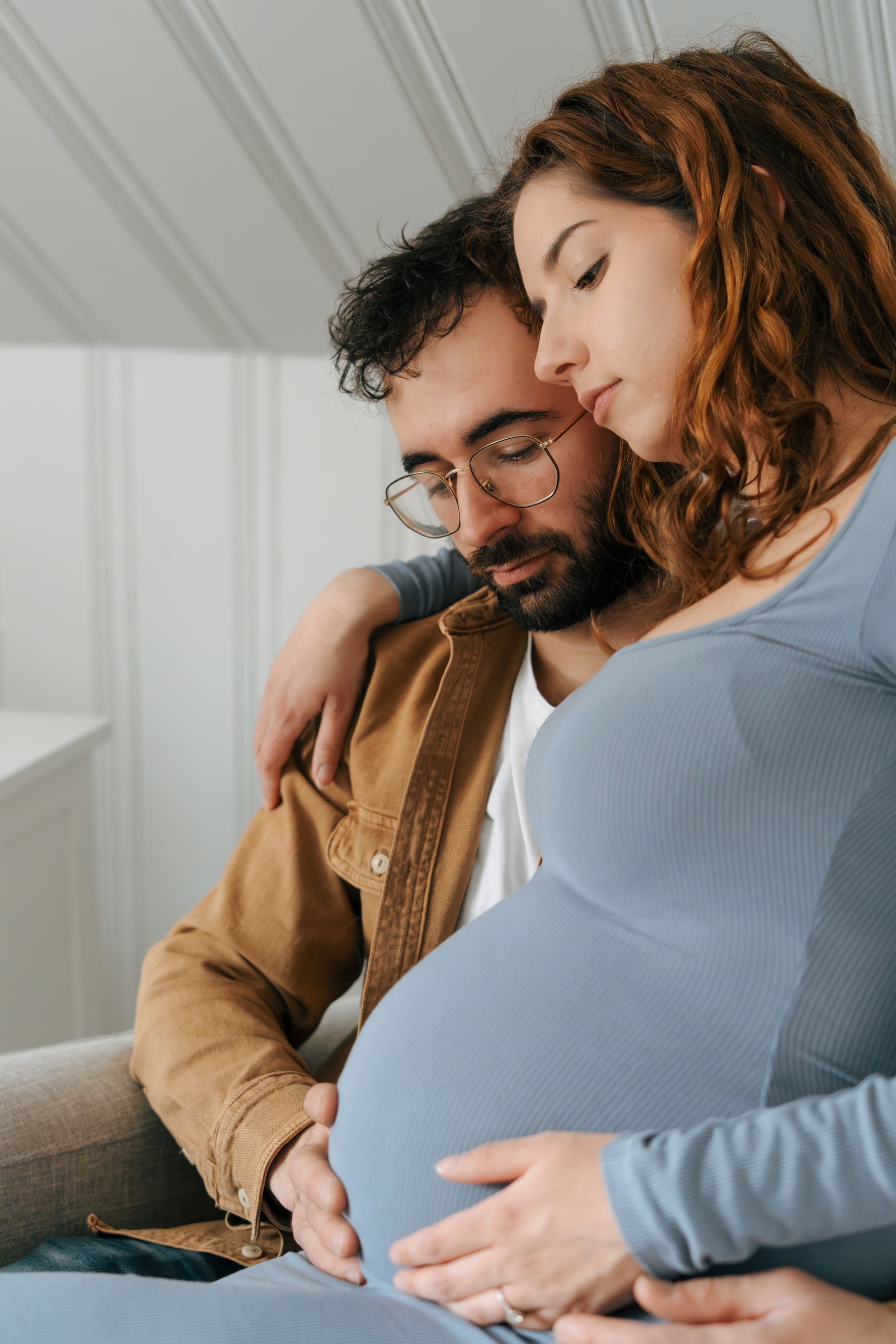 Couple shares intimate moment together as they rest hands on her pregnant belly in tender indoor portrait.
