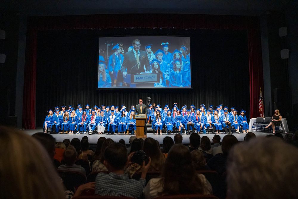NPA Superintendent David Lykins addresses graduates at the podium with students who delivered welcome portions in Spanish and Diné.