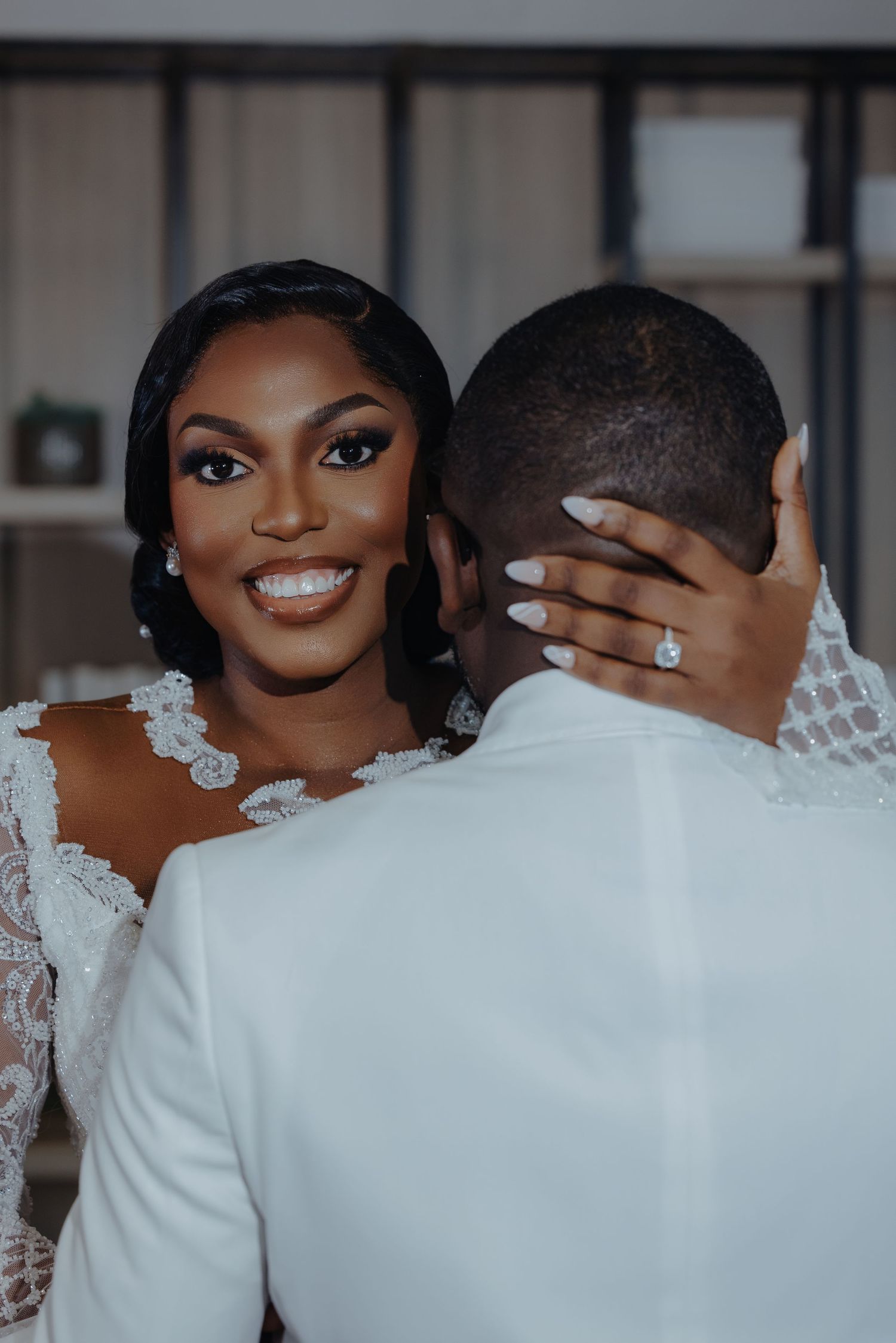 A romantic wedding portrait showing a bride in a lace dress smiling while the groom turns away from camera.