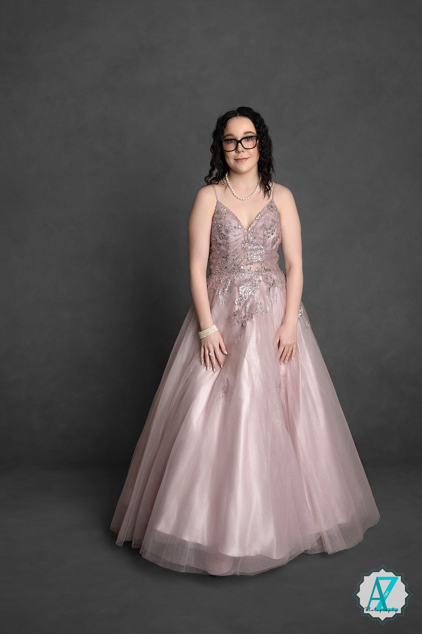 Elegant blush pink ball gown with sparkly embellishments and tulle skirt photographed against dark gray backdrop.