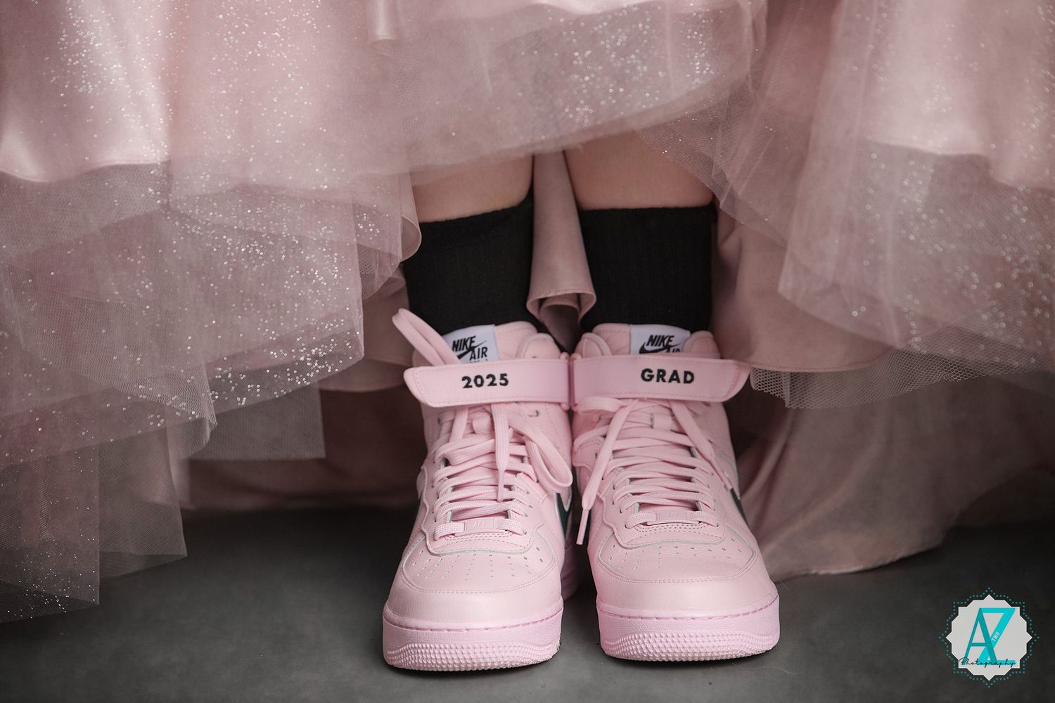Custom pink Nike Air Force 1 sneakers with 'Best Grad' text paired with flowing tulle dress in soft pink tones.