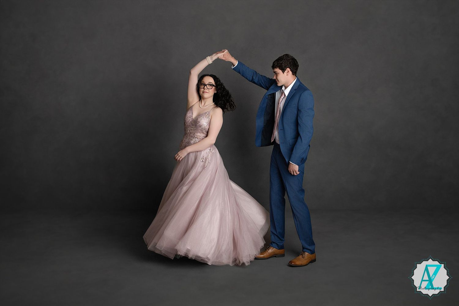 A couple in formal attire performs an elegant dance pose against a dark gray backdrop.