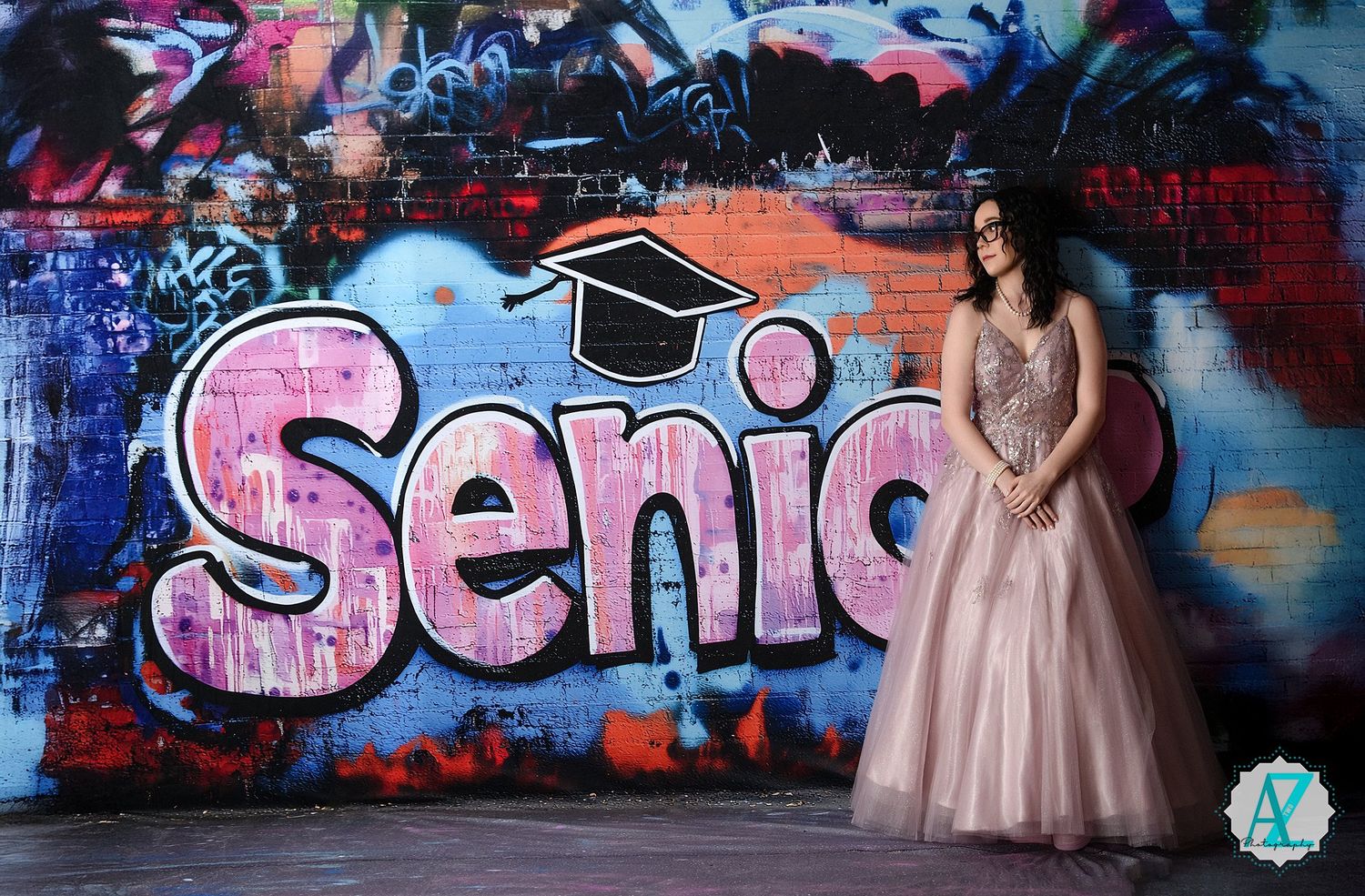 A senior portrait taken against a colorful graffiti wall featuring a 'Senior' graduation cap design.