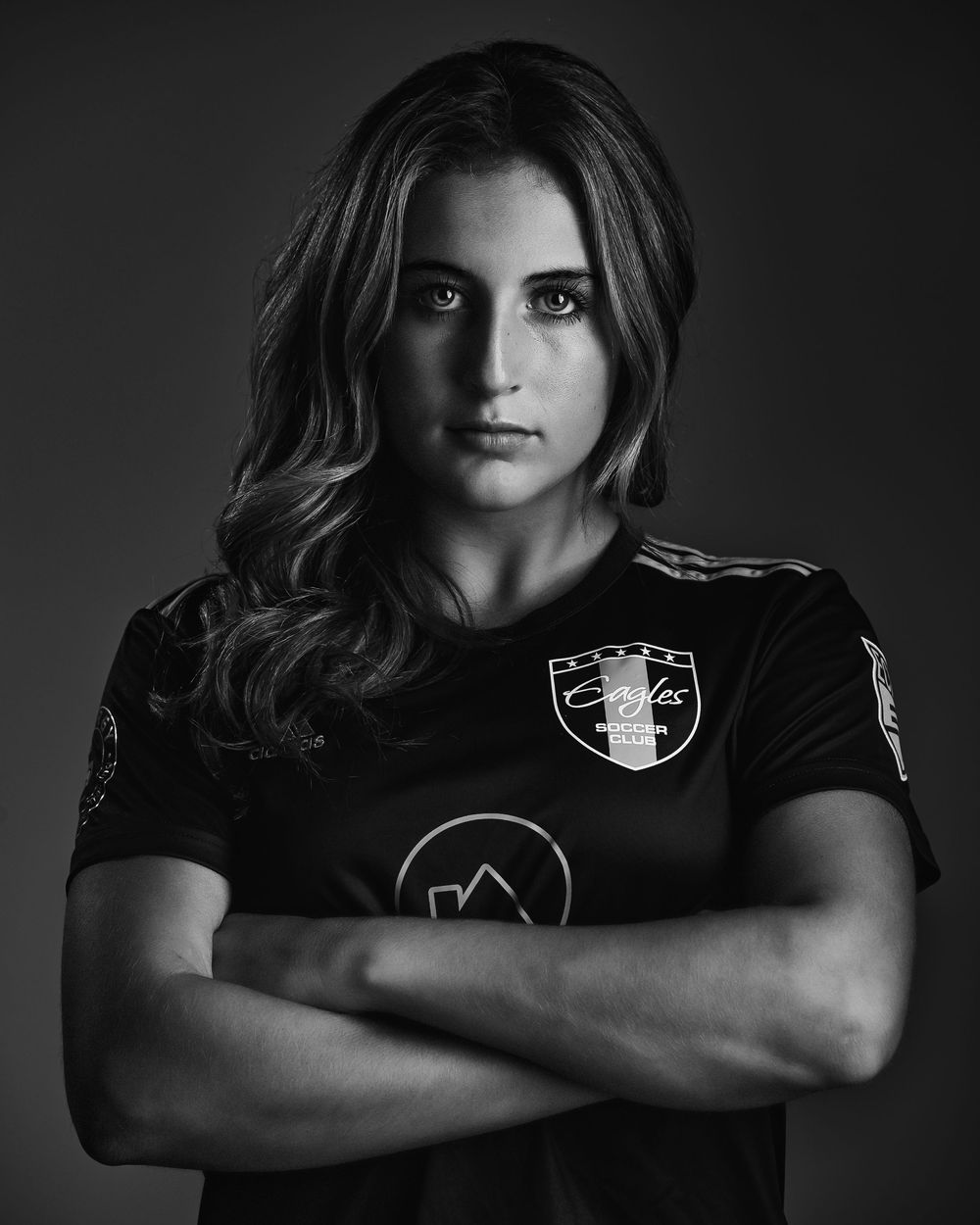 Black and white portrait of female soccer player with arms crossed in dark uniform.