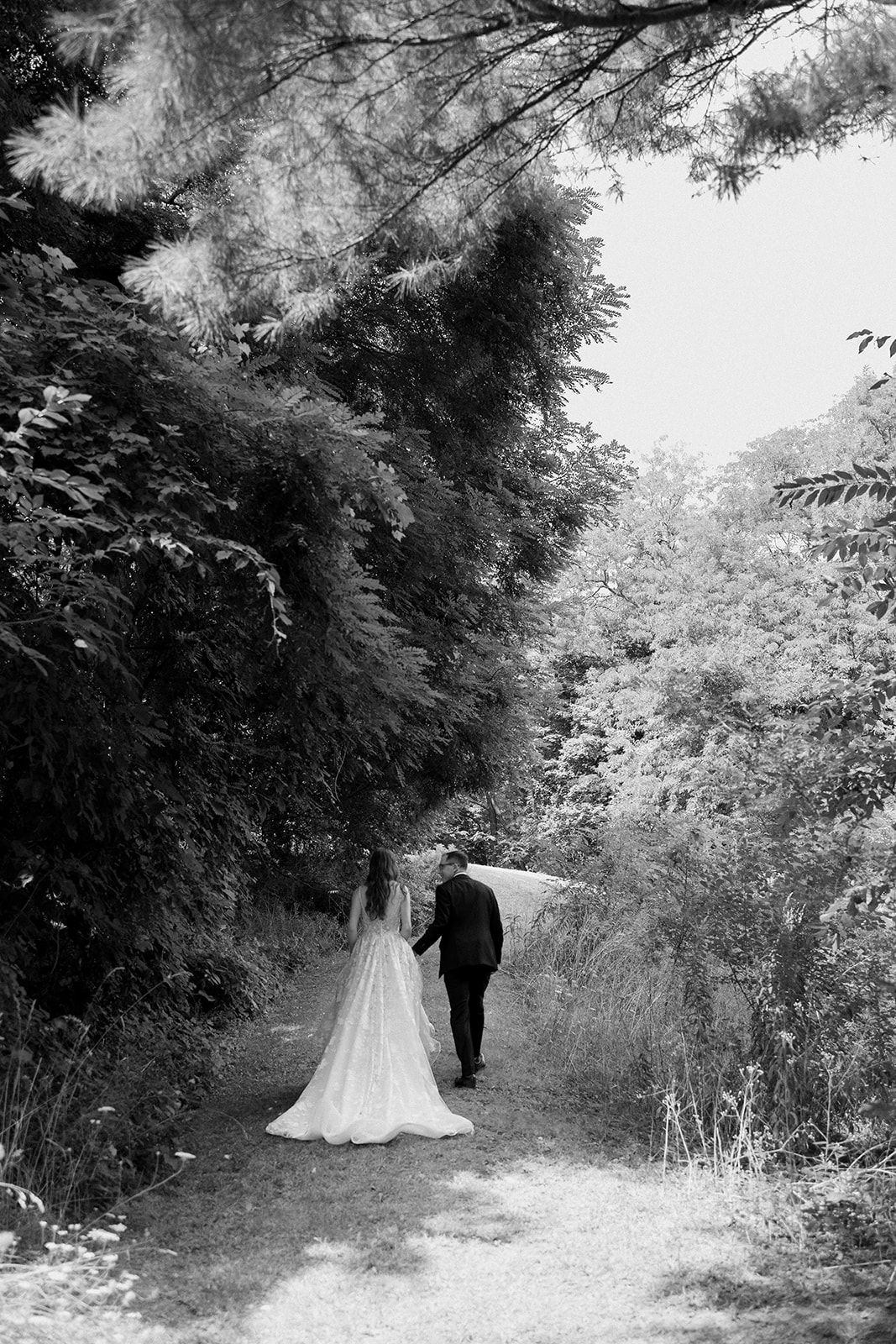 A couple walking down a tree-lined path in black and white photography.