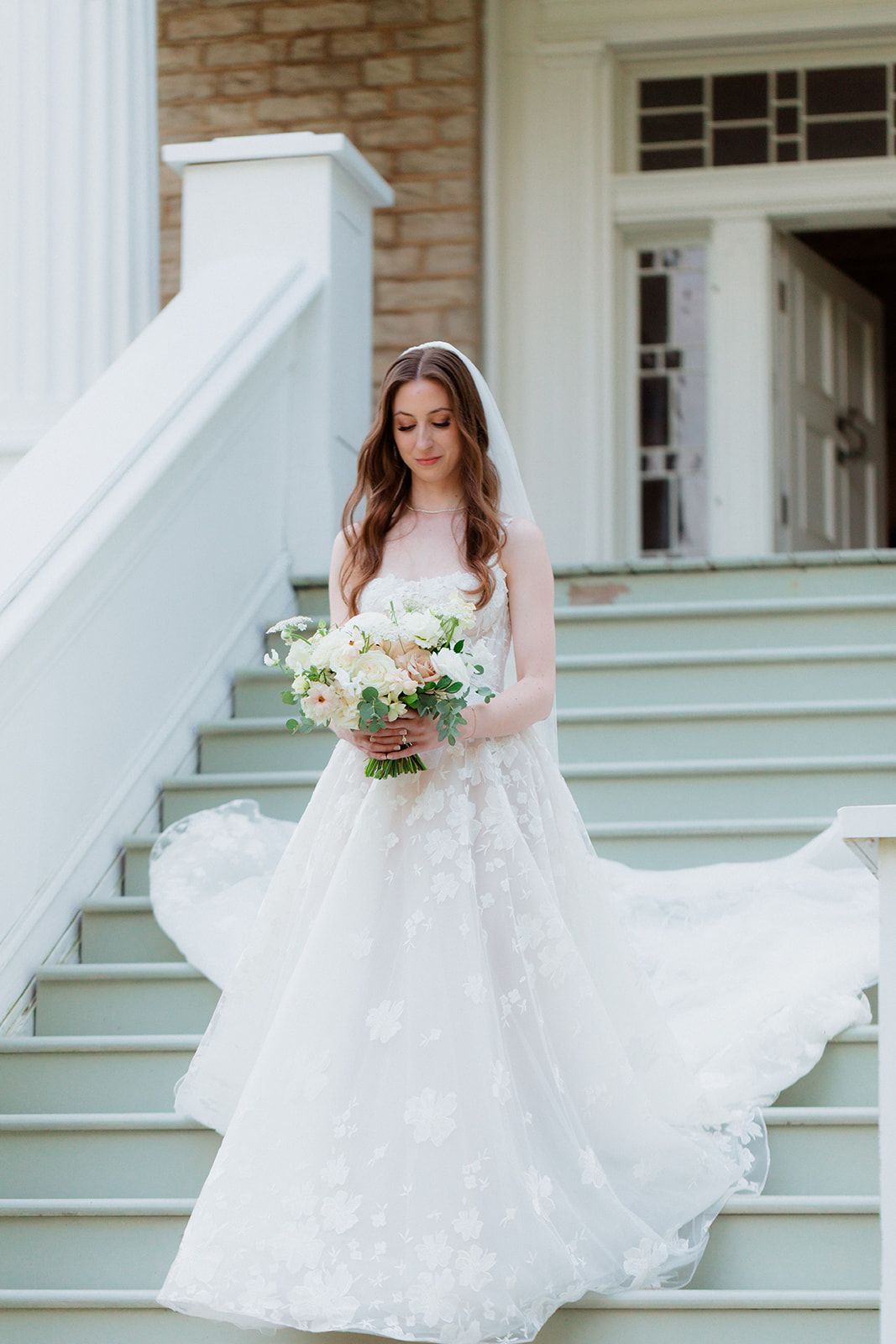 A white wedding dress flowing elegantly on outdoor stairs with a bouquet.