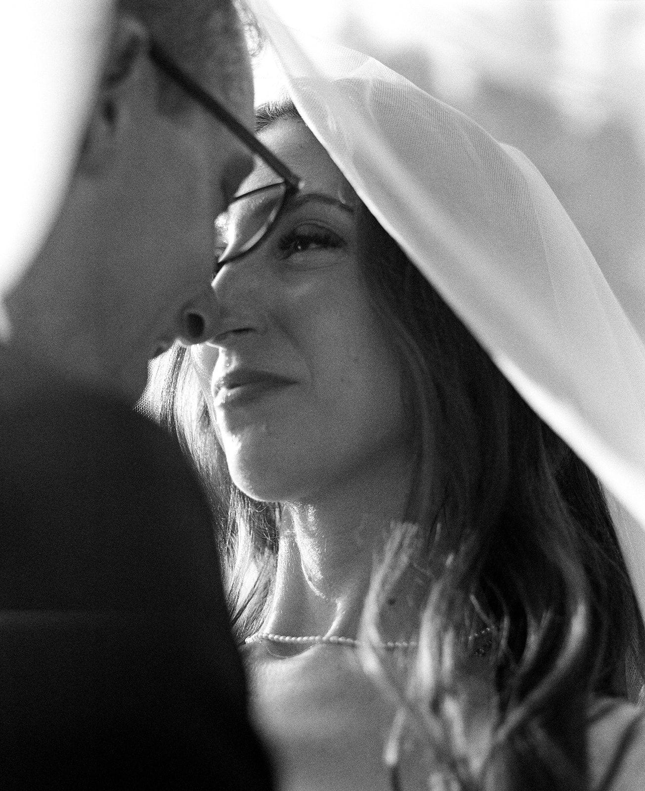 Artistic black and white close-up of a bride's profile through delicate wedding veil fabric.