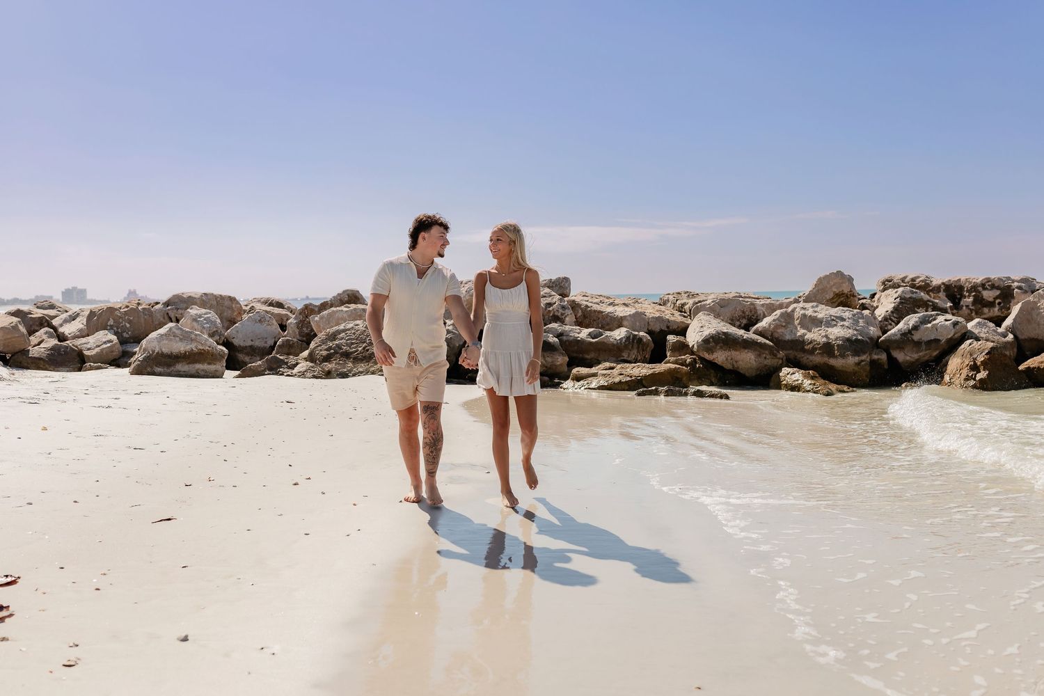 Distant view of couple on rocky beach against blue sky.