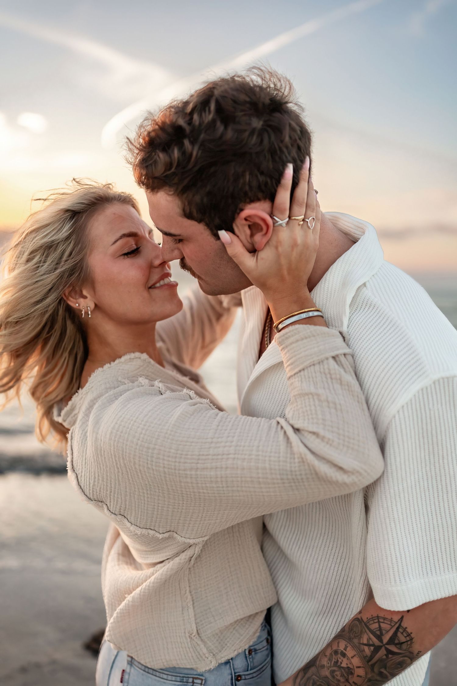 Romantic couple in neutral sweaters sharing intimate moments on a beach at sunset.
