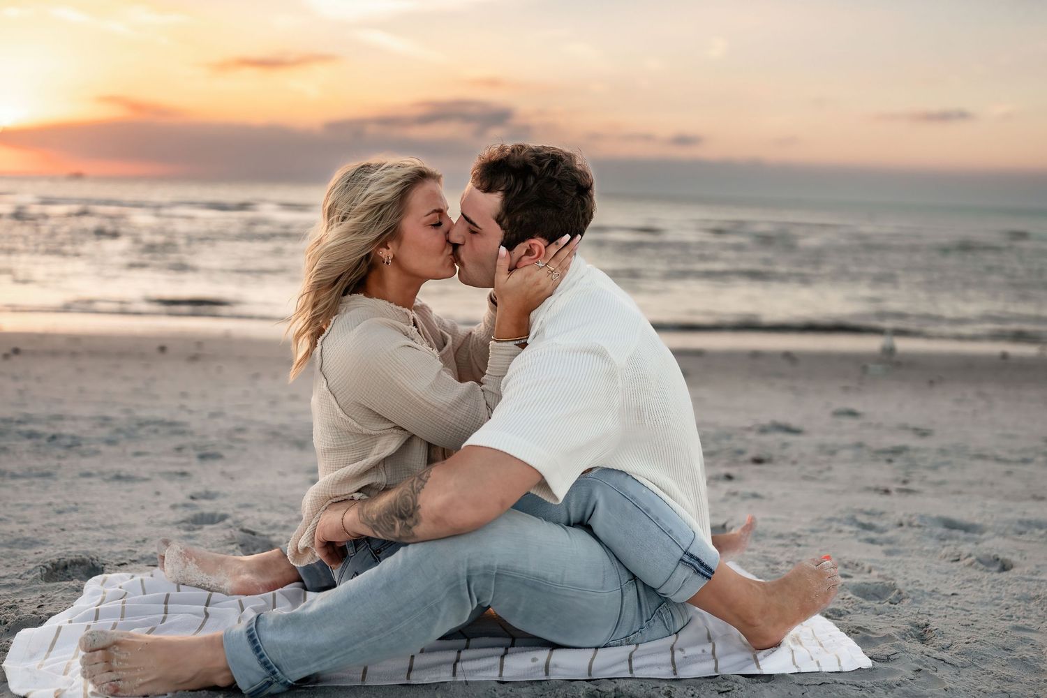 Couple embracing tenderly on sandy beach during golden hour.