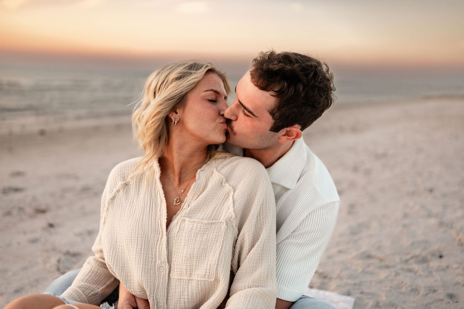 Intimate beach photoshoot featuring couple in coordinated cream and white outfits.