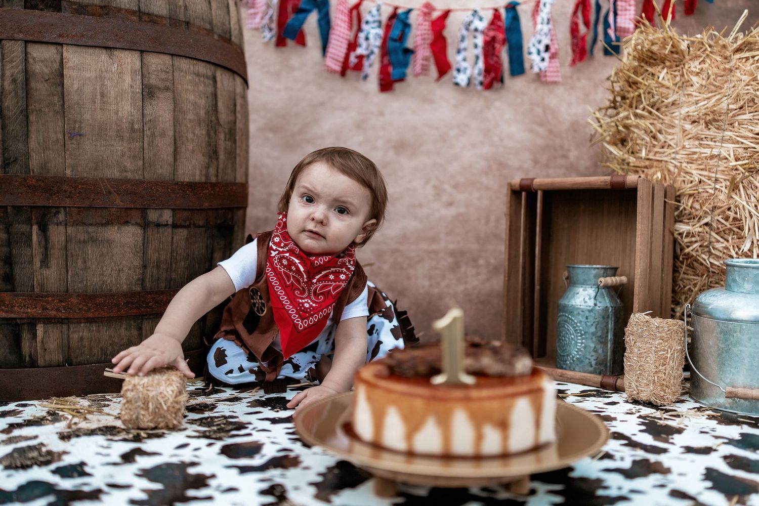 Rustic first birthday party scene with western decor and cake on cow print tablecloth.